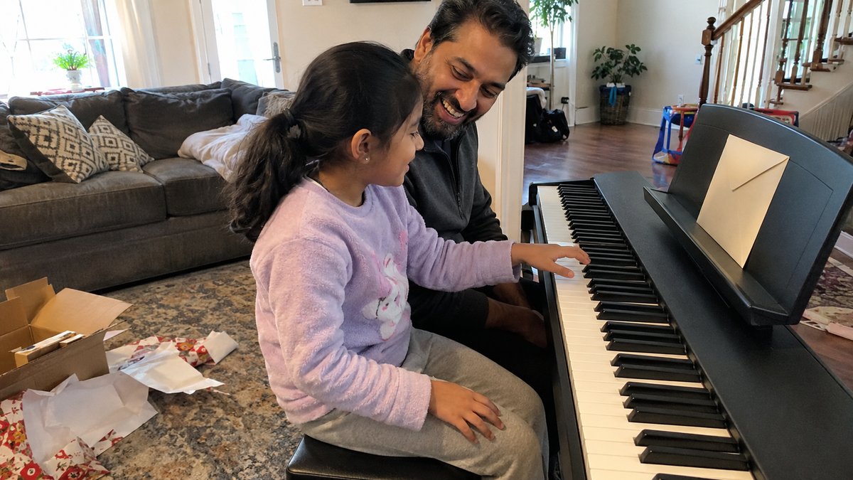 Father and young daughter seated together at a new digital keyboard with a gift envelope nearby
