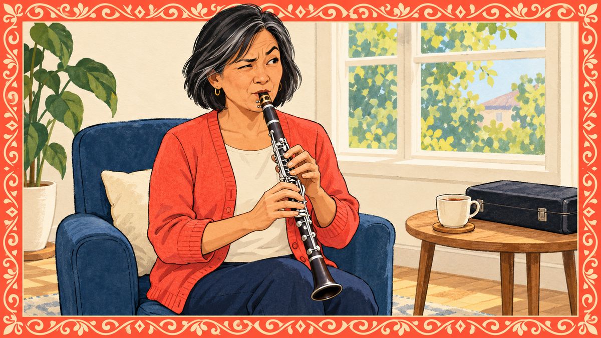 A woman in a coral cardigan plays the clarinet in her armchair, wincing a little at a squeak